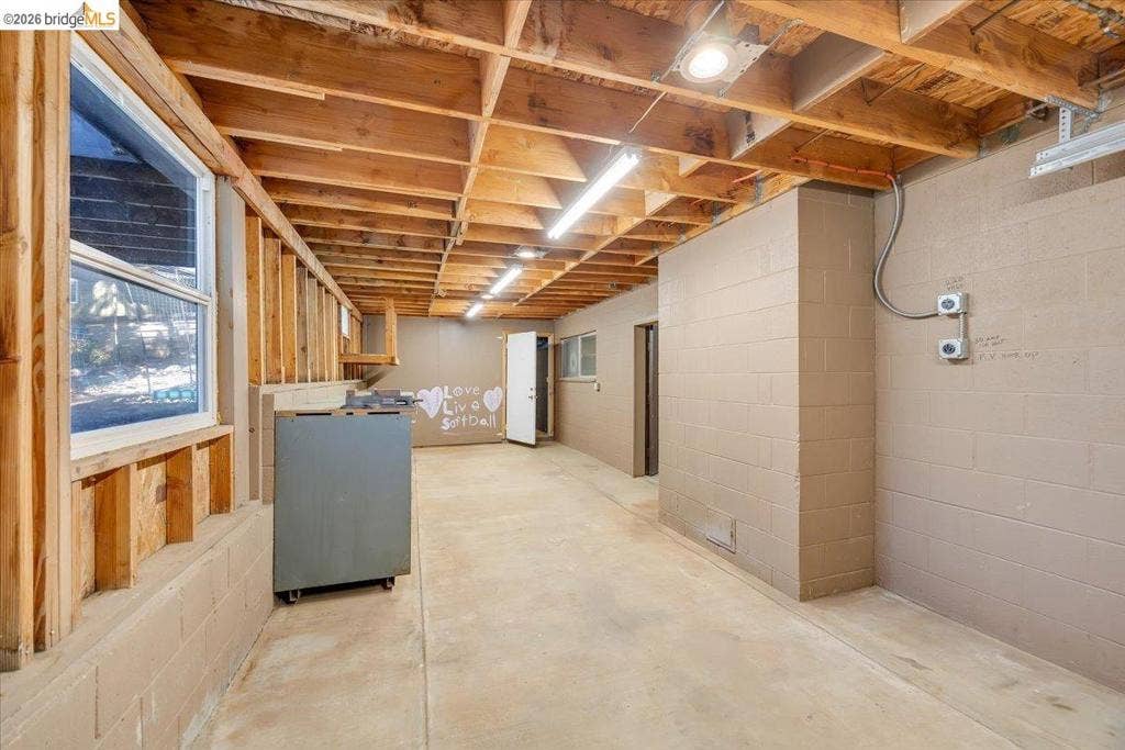 5827 Lookout Ct, CA 95233 Unfinished lower level featuring exposed wood joist ceilings, concrete block walls, concrete flooring, and linear light fixtures