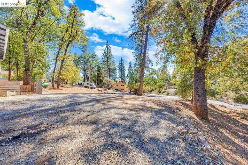 5827 Lookout Ct, CA 95233 Spacious gravel parking area accented by mature pine and deciduous trees on a sloped lot