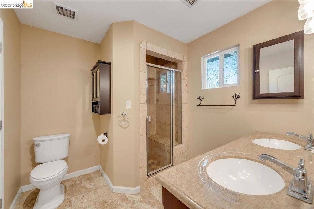 5827 Lookout Ct, CA 95233 Double vanity with a solid-surface countertop and integrated sinks, walk-in shower featuring a tiled surround and built-in bench, and wall-mounted cabinetry
