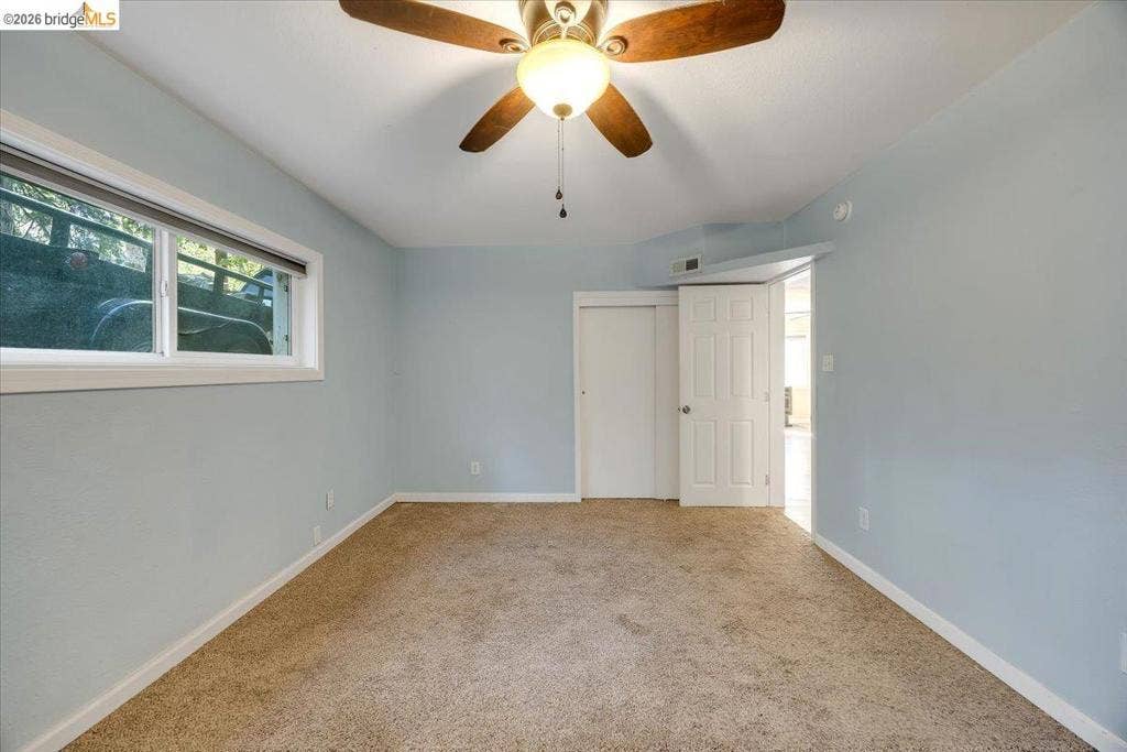 5827 Lookout Ct, CA 95233 Room featuring wall-to-wall carpeting, a ceiling-mounted fan with integrated light fixture, a window with white trim, and a six-panel interior door