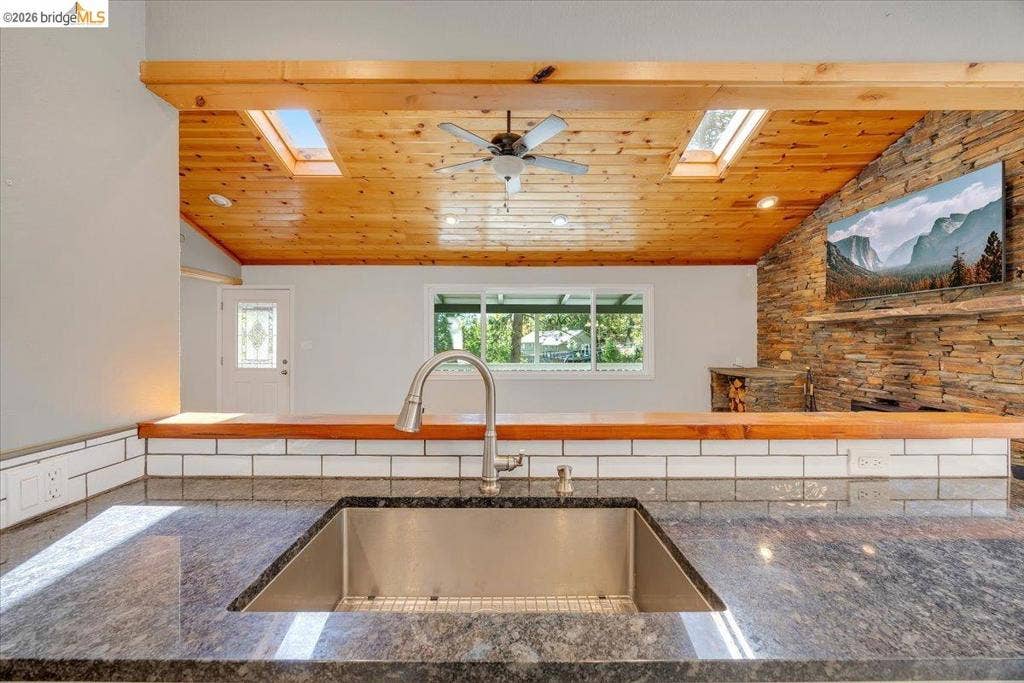 5827 Lookout Ct, CA 95233 Kitchen featuring a stone-finish countertop with a stainless steel undermount sink, white subway tile backsplash, wood-plank vaulted ceiling with skylights, and a natural stone accent wall
