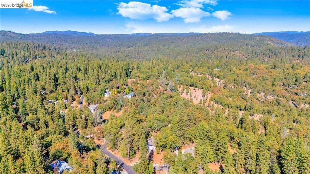5827 Lookout Ct, CA 95233 Aerial perspective of a wooded landscape featuring mature evergreen and deciduous trees, mountainous terrain, and asphalt roadway access