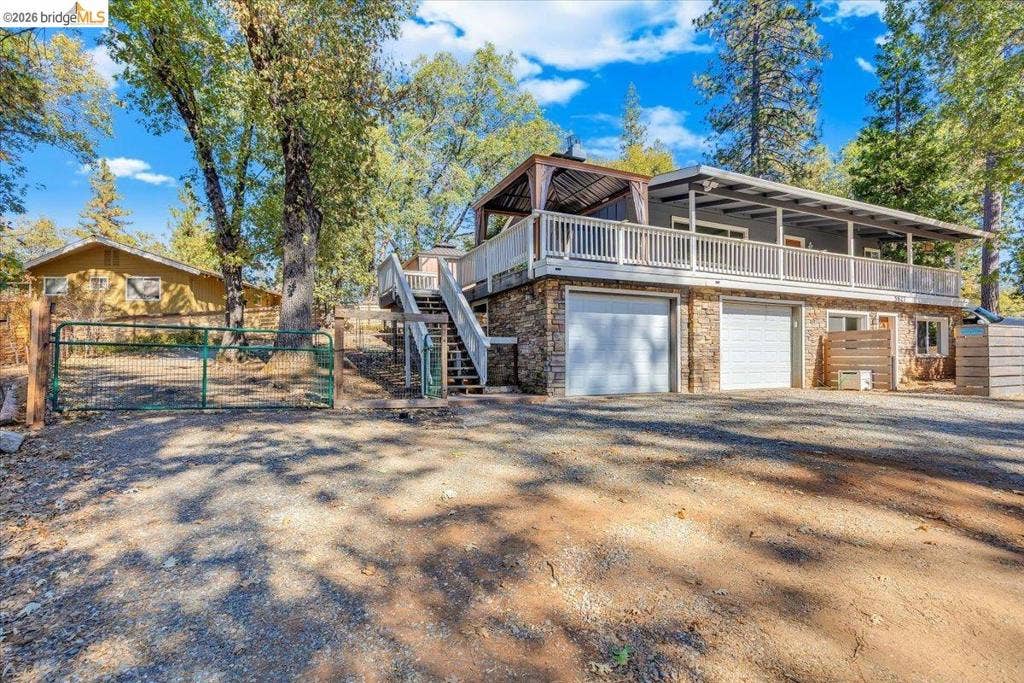 5827 Lookout Ct, CA 95233 Two-story residence featuring natural stone veneer lower-level siding, dual garage doors, a wraparound deck with white railing, and an exterior staircase