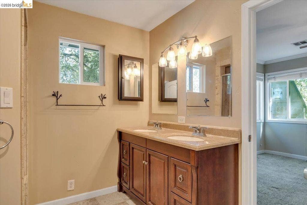5827 Lookout Ct, CA 95233 Double vanity featuring a stone-composite countertop, dual undermount sinks, wood cabinetry, wall-mounted medicine cabinet, and a multi-bulb light fixture