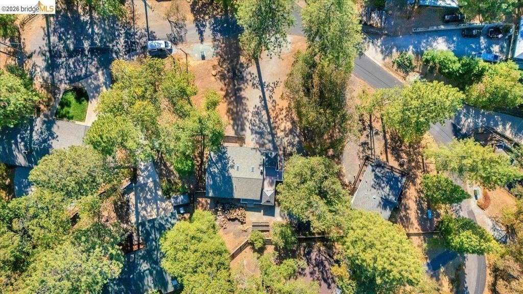 5827 Lookout Ct, CA 95233 Aerial perspective of a multi-structure property featuring mature evergreen trees, a paved driveway, and detached storage outbuildings