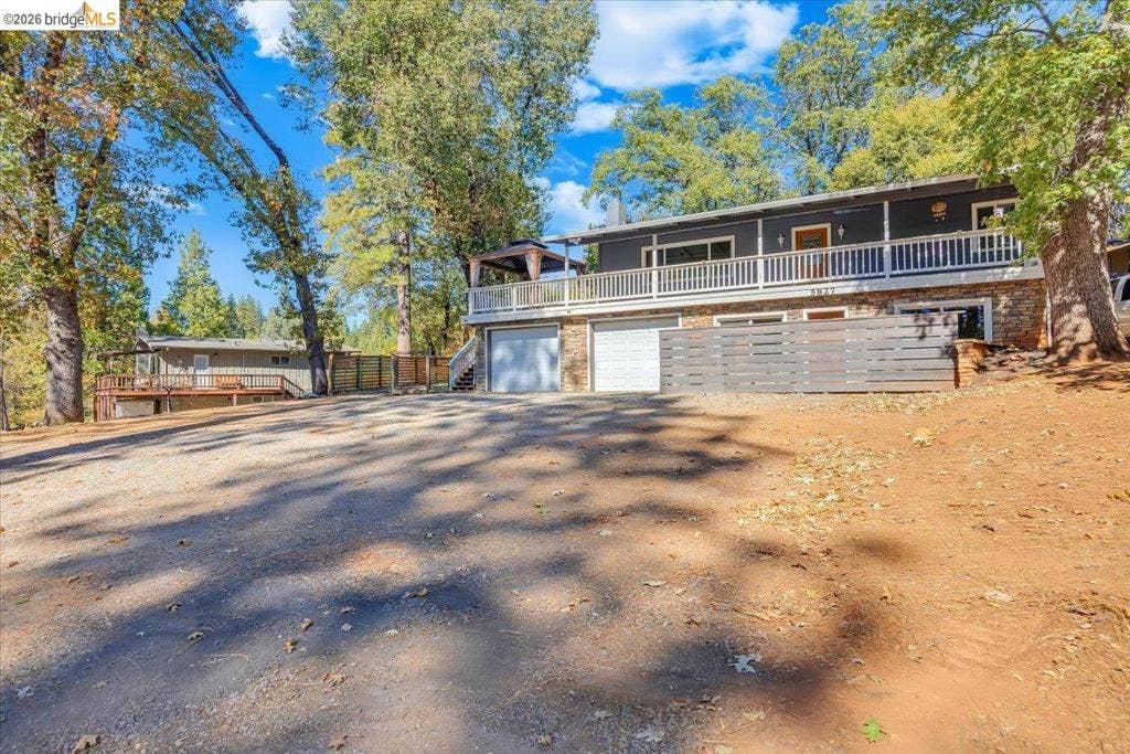 5827 Lookout Ct, CA 95233 Two-story residence featuring an expansive wrap-around deck with white railing, stone lower-level exterior, two-car garage, and horizontal wood privacy fencing