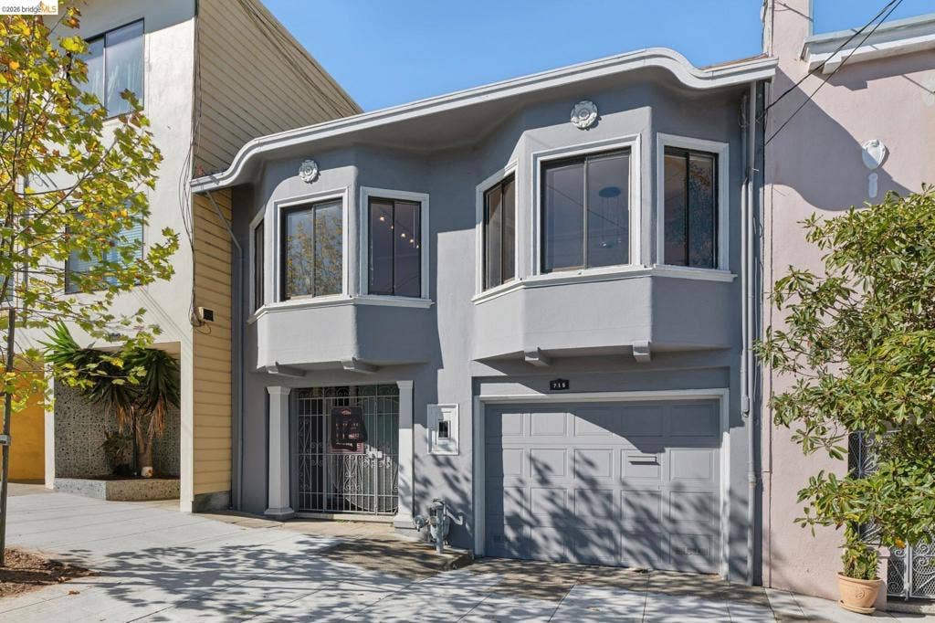 715 17Th Ave, San Francisco, CA 94121 Exterior facade featuring a smooth stucco finish, dual upper-level bay windows, decorative crown medallions, a metal security gate, and an integrated single-car garage