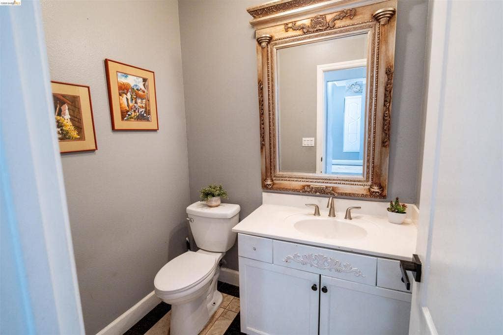4600 Via Terreno, Modesto, CA 95357 White vanity with a carved drawer panel, integrated basin, dual-handle brushed metal faucet, and an ornate, detailed frame mirror