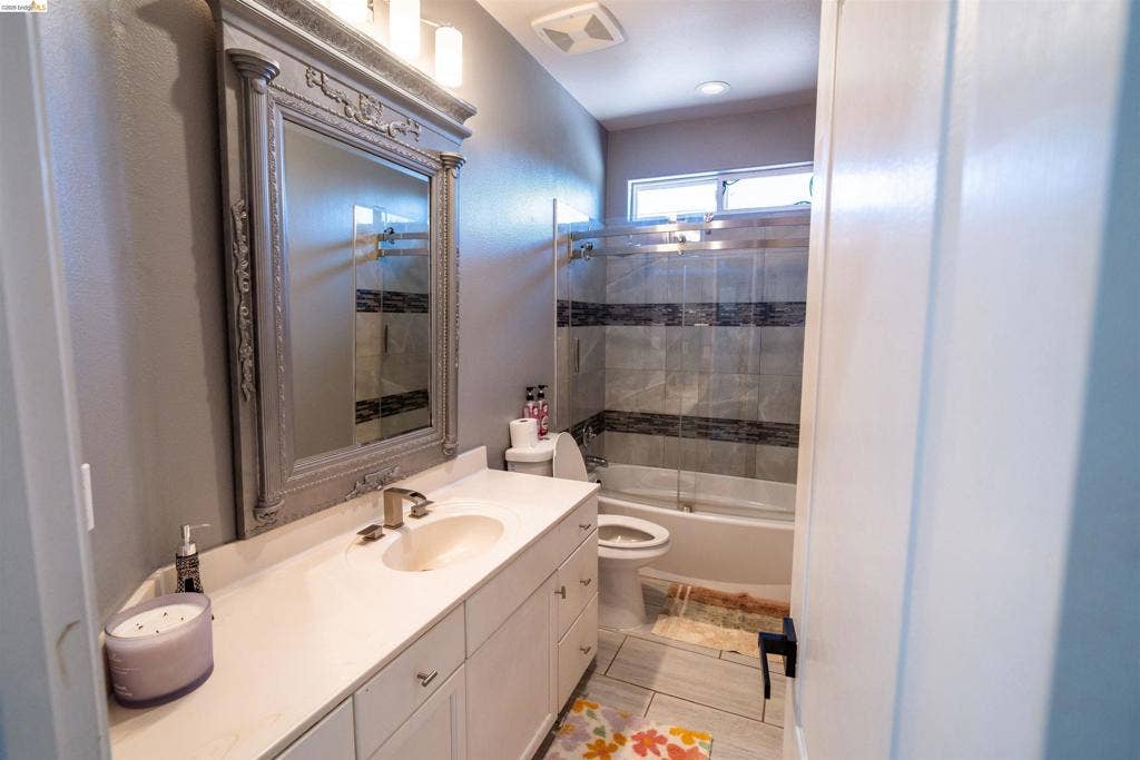 4600 Via Terreno, Modesto, CA 95357 Bathroom featuring a vanity with a white countertop and oval sink, a wall-mounted decorative frame mirror, recessed lighting, and a bathtub with a glass shower enclosure and tiled surround