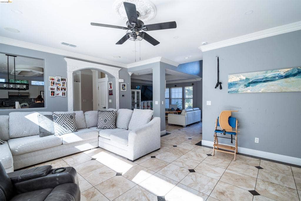 4600 Via Terreno, Modesto, CA 95357 Living area featuring tile flooring with dark accent insets, crown molding, a central ceiling fan with a decorative medallion, and arched architectural detailing