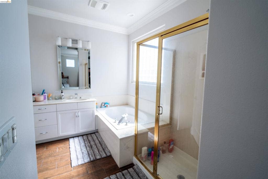 4600 Via Terreno, Modesto, CA 95357 Bathroom featuring white cabinetry, built-in soaking tub with a stone-finish surround, glass-enclosed shower with gold-tone frame, and wood-finish flooring