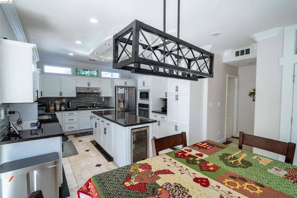 4600 Via Terreno, Modesto, CA 95357 Kitchen featuring white shaker-style cabinetry, dark stone countertops, a central island with an integrated beverage refrigerator, geometric metal pendant lighting, and tiled flooring