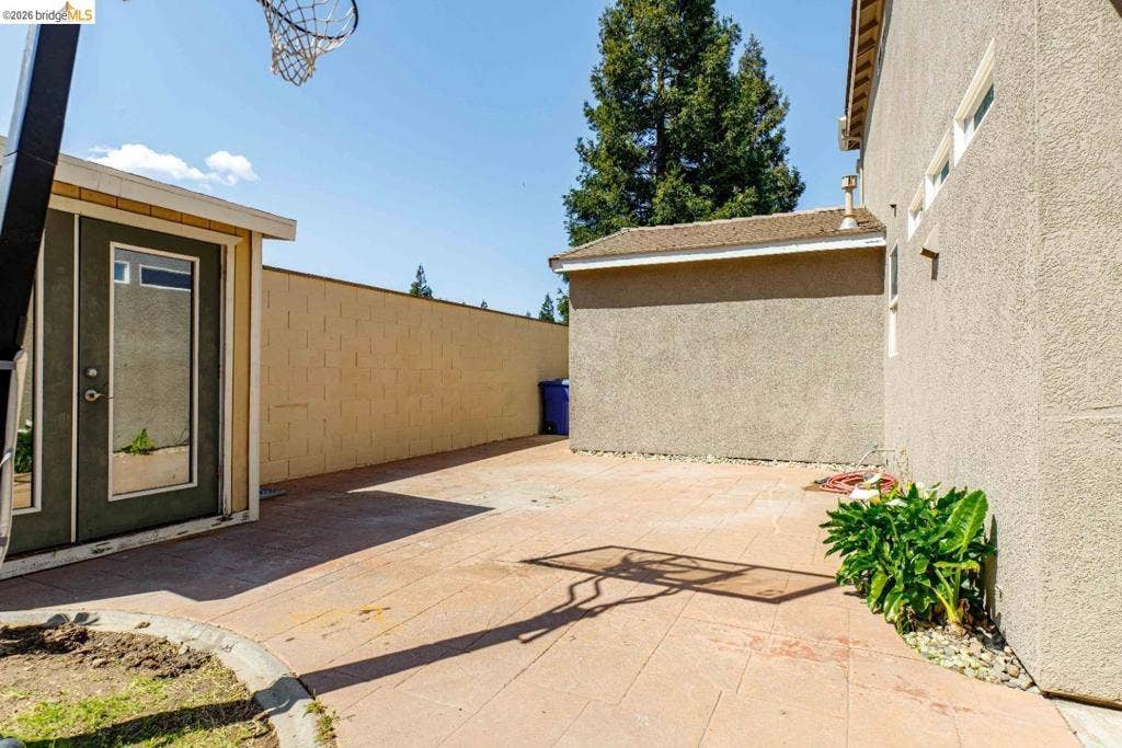 4600 Via Terreno, Modesto, CA 95357 Side yard featuring concrete paver patio, stucco exterior walls, perimeter masonry wall, and mature coniferous trees