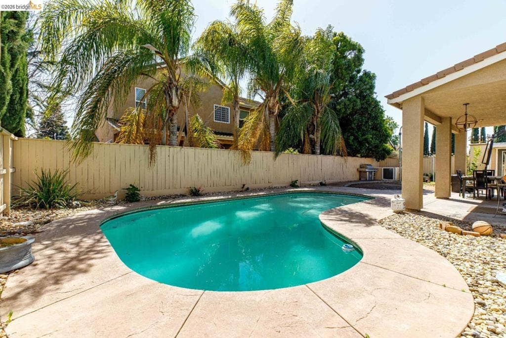 4600 Via Terreno, Modesto, CA 95357 In-ground swimming pool featuring a curved concrete deck, covered patio, and perimeter privacy fencing
