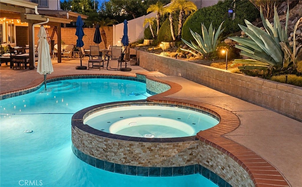 2400 Pepperwood, Corona, CA 92882 A resort-style backyard with sparkling pool, elevated spa, mature tropical landscaping, and warm evening landscape lighting.