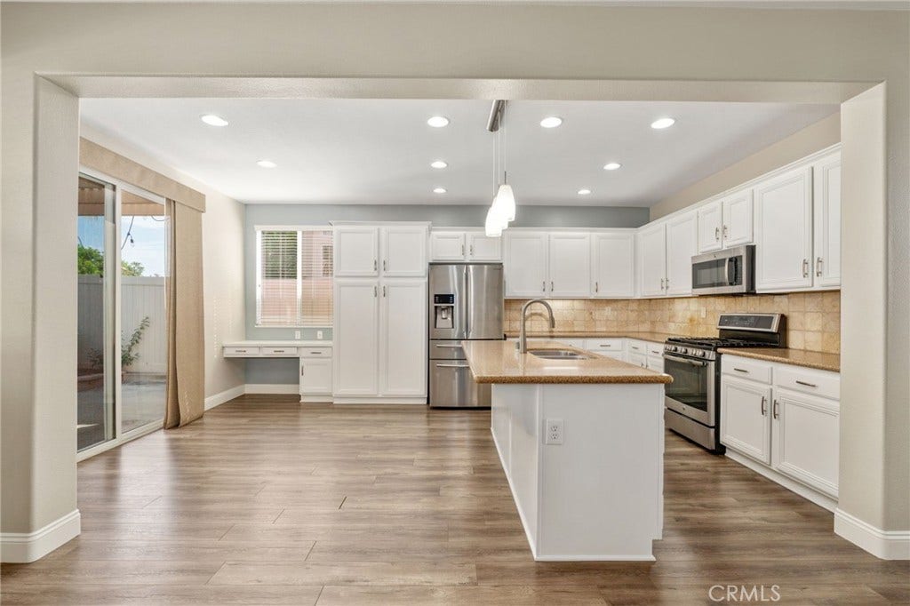 32440 Magenta Court, Temecula, CA 92592 Spacious Kitchen And Adjacent Dining Area Featuring White Cabinetry, Stainless Steel Appliances, A Large Center Island, Recessed Lighting, And Sliding Glass Door Access To The Backyard.