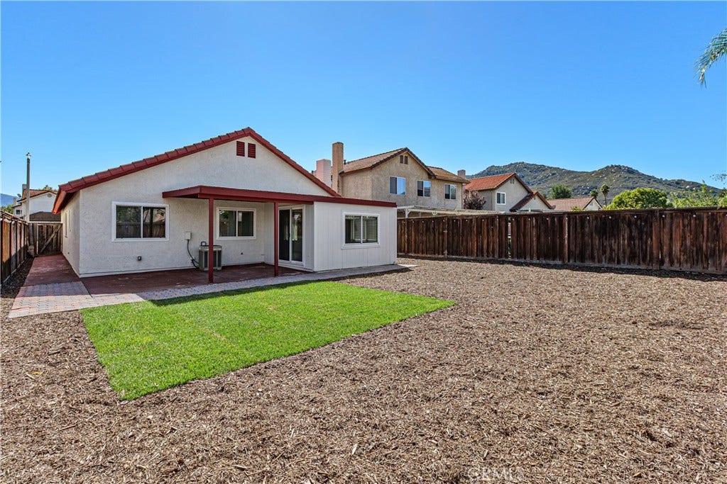42329 Via Consuelo, Temecula, CA 92592 Rear exterior view showcasing the covered patio, green lawn area, and low-maintenance landscaping within the fenced backyard.