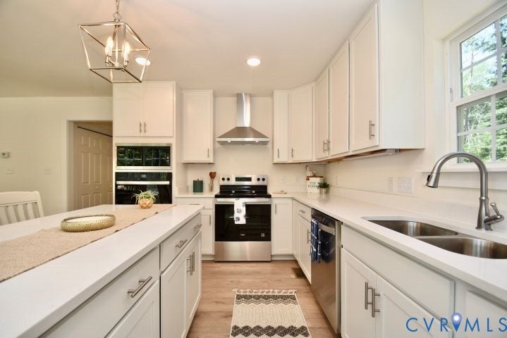 54 Porkchop Court, Louisa, VA 23093 Well-appointed kitchen featuring white cabinetry, light-toned countertops, stainless steel appliances, a center island with built-in storage, and wood-finish flooring