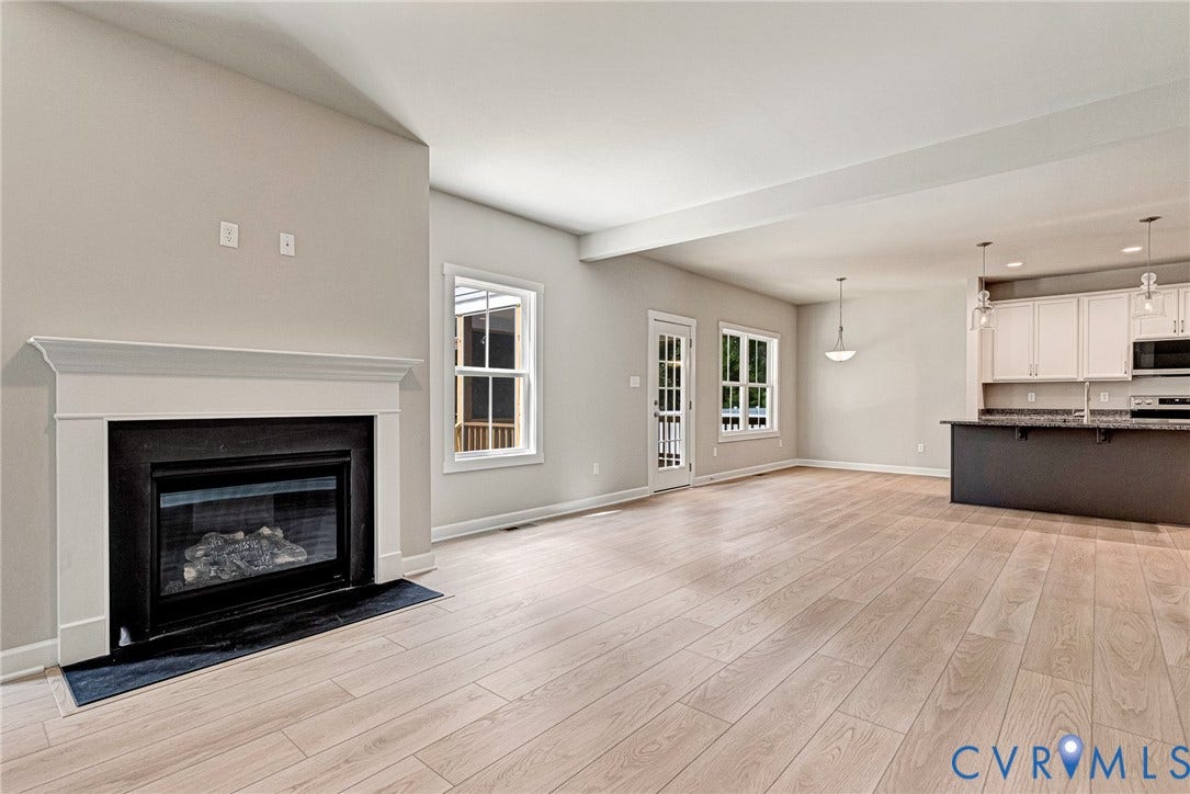 Wood-finish flooring, white mantel fireplace with a black surround, white trim windows, white shaker cabinetry, and pendant lighting