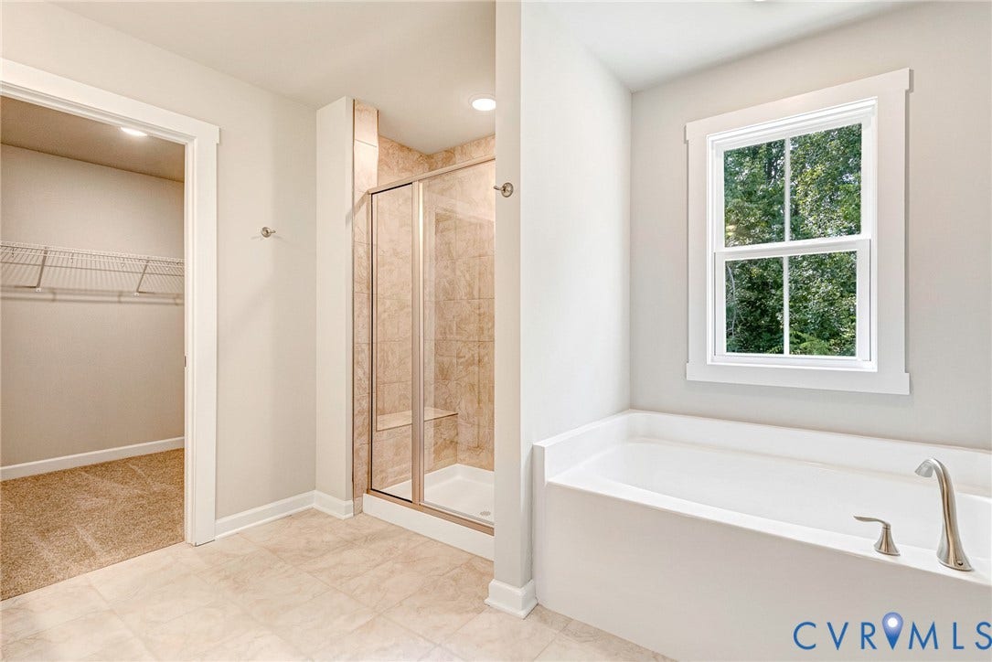 Spacious bathroom featuring a full-size soaking tub with brushed nickel fixtures, a glass-enclosed shower with tiled walls and built-in bench, and light-toned floor tile
