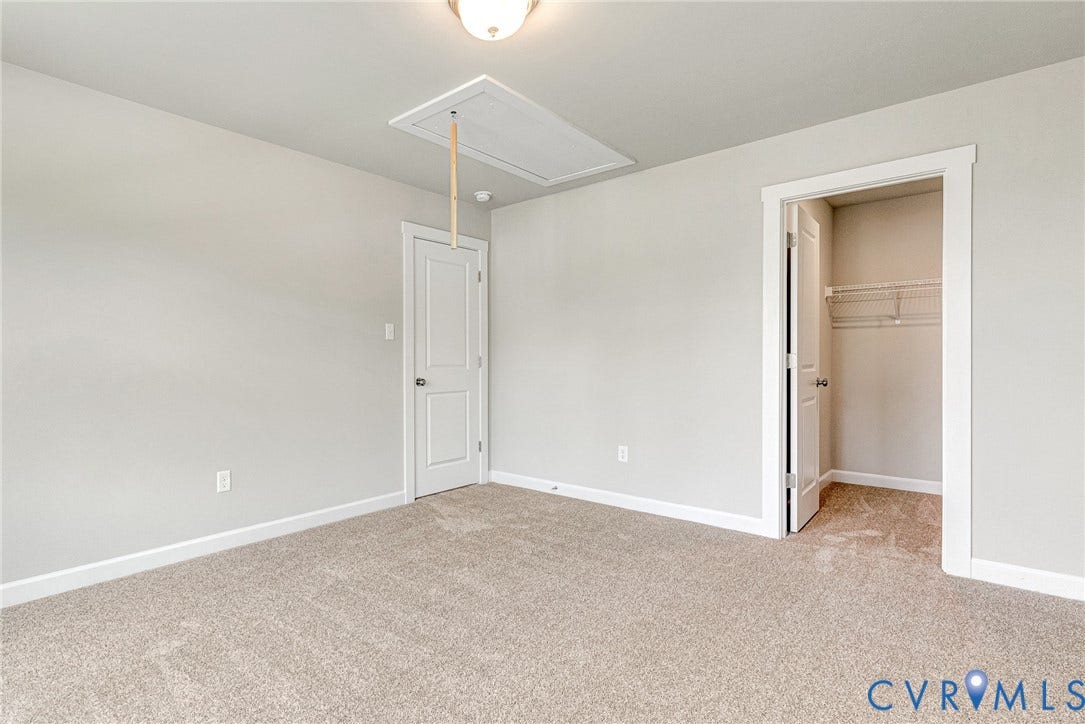 Neutral wall paint, plush carpet, white trim, attic access, and a closet with wire shelving