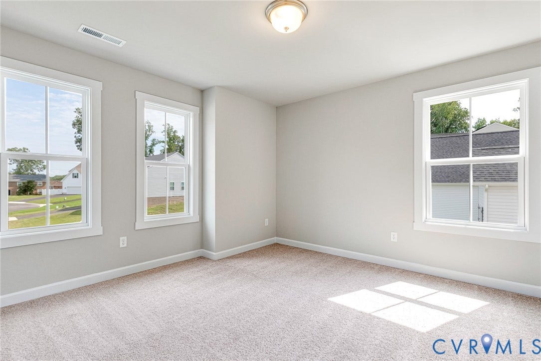 Neutral wall tones, three large windows, recessed ceiling light fixture, and light-colored carpeting
