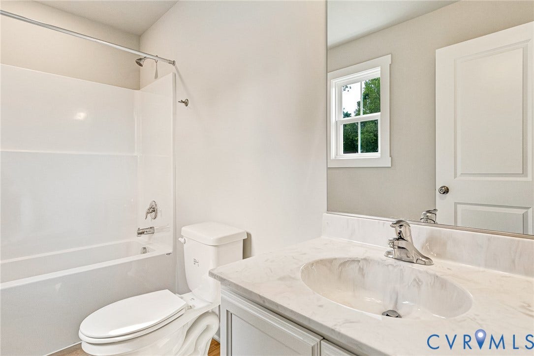 Bathroom featuring a shower-tub combination, vanity with single basin sink, and a framed window