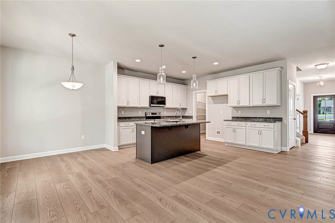 Kitchen featuring white cabinetry, dark island with a sink, stainless steel appliances, and wood-finish flooring
