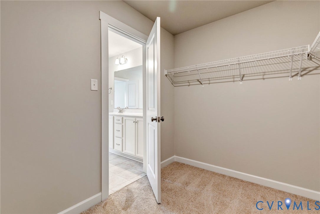 Carpeted room with wire shelving, offering direct access to a bathroom featuring a vanity with shaker-style cabinetry, a built-in sink, and wall-mounted light fixtures