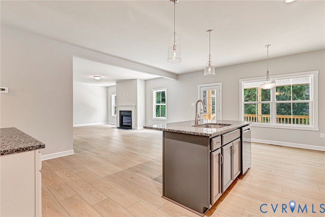 Kitchen featuring wood-finish flooring, white cabinetry, granite countertops, and a center island with sink