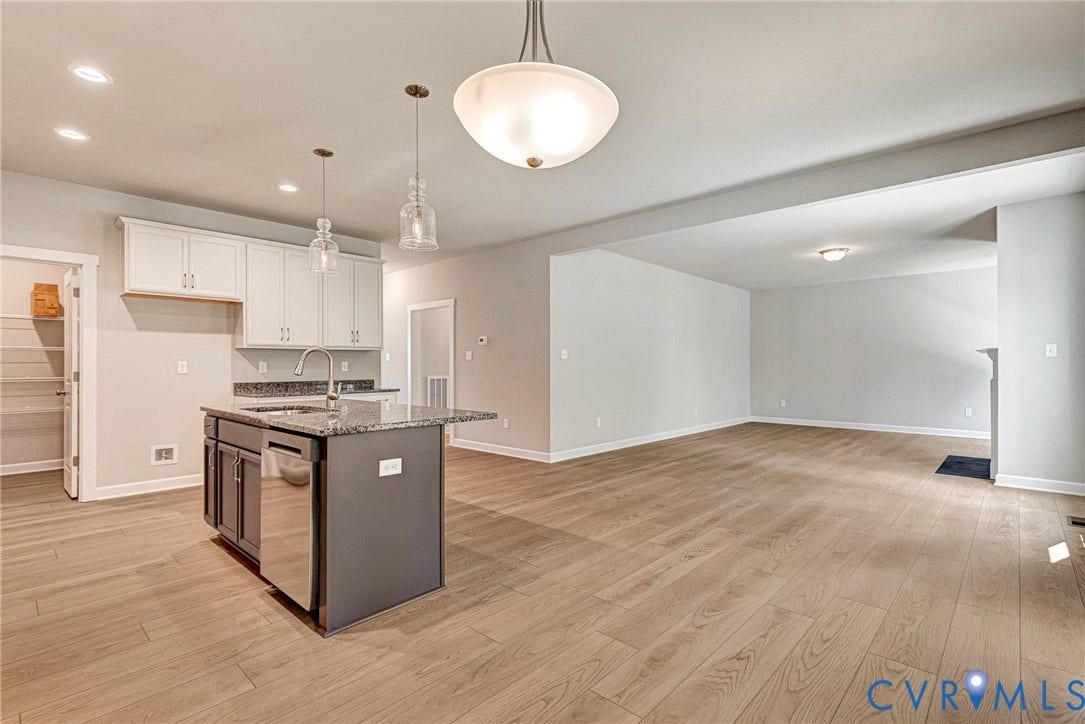 Open-concept kitchen and living area featuring wood-finish flooring, a kitchen island with integrated sink, stainless steel appliances, and a built-in fireplace