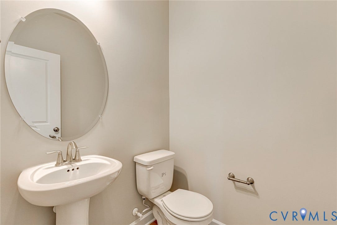 Pedestal sink with a brushed nickel faucet, oval frameless mirror, and a ceramic toilet