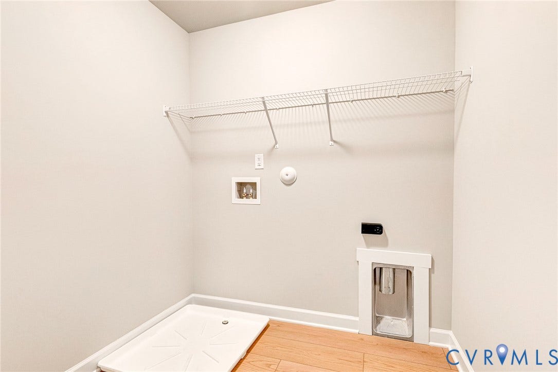 Laundry space featuring wood-finish flooring, white wire shelving, and a washing machine pan