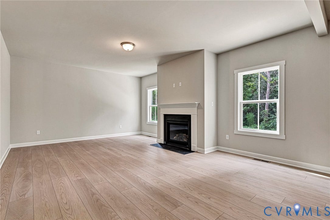 Spacious living area featuring wood-finish flooring, a fireplace with a mantel, and multiple windows