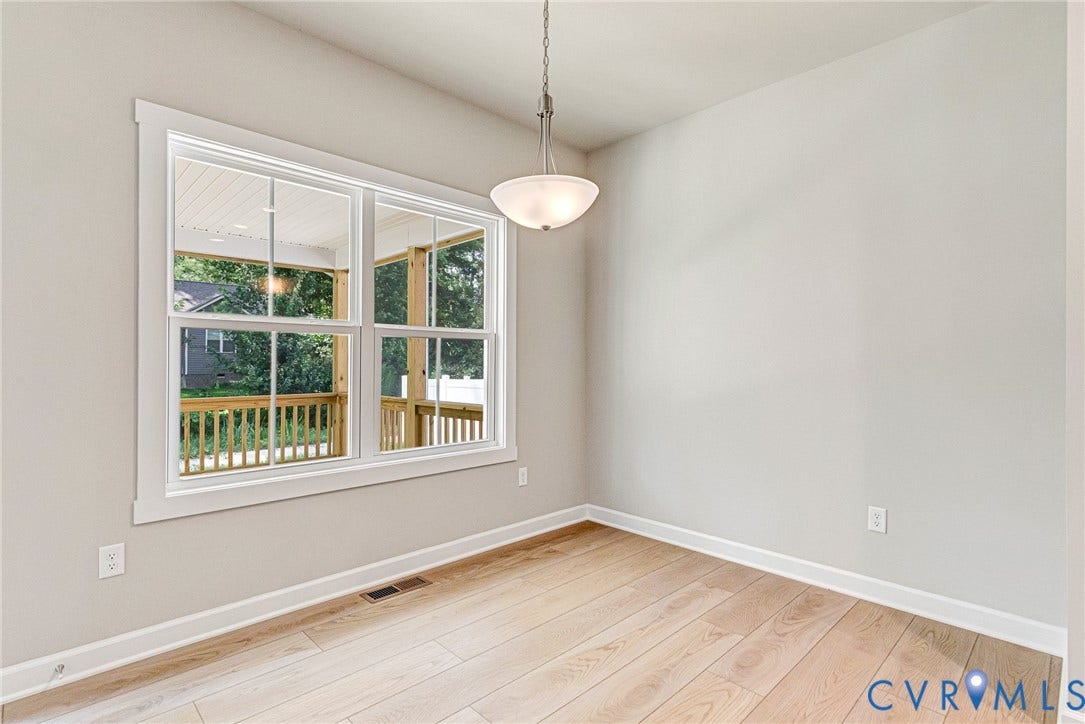 Open-concept living space featuring wood-finish flooring, a fireplace with a white mantel, and a kitchen with an island, light cabinetry, and pendant lighting