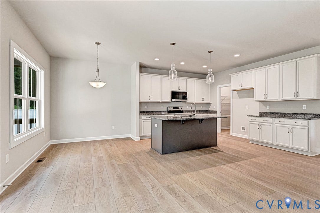 Spacious interior with wood-finish flooring, white cabinetry, dark stone countertops, and a kitchen island