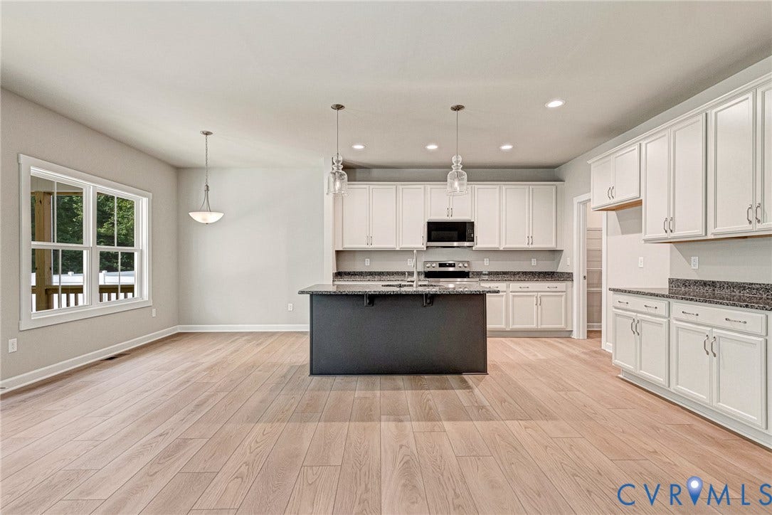 Open-concept living space featuring wood-finish flooring, a kitchen island with seating, pendant lighting, recessed lighting, and white cabinetry