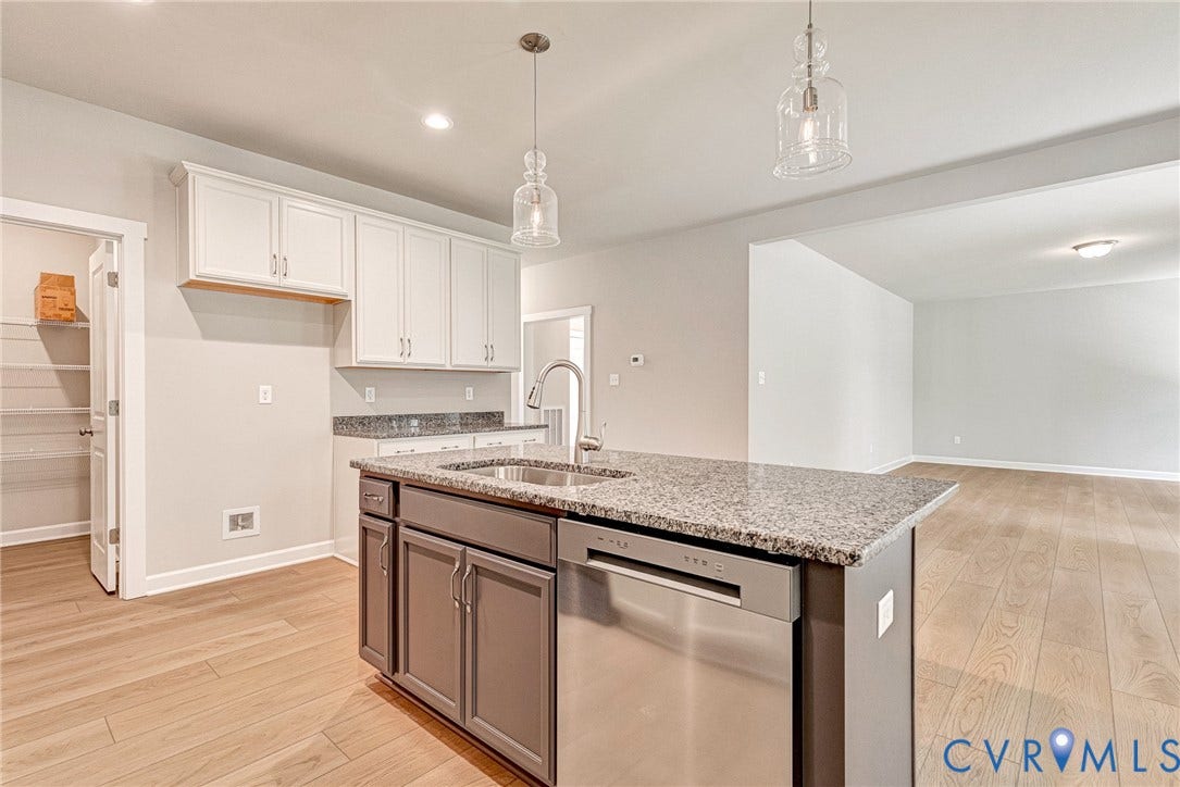 Spacious kitchen and dining area featuring light wood-finish flooring, white cabinetry, dark granite-style countertops, stainless steel appliances, and a central island with an undermount sink