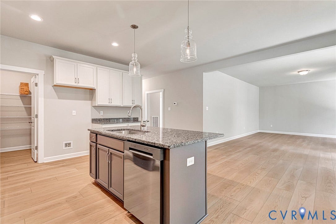 Open-concept kitchen and living area featuring wood-finish flooring, a kitchen island with integrated sink, stainless steel appliances, and a built-in fireplace