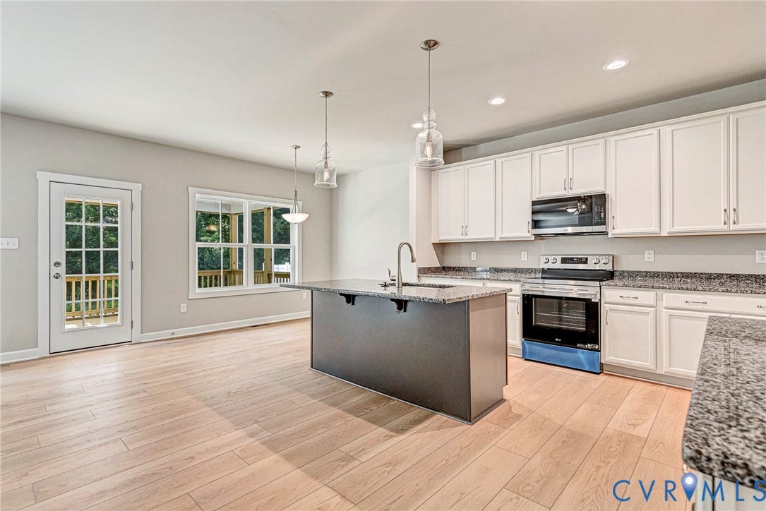 Light wood-finish flooring, a central fireplace with a white mantel, and multiple windows define this space