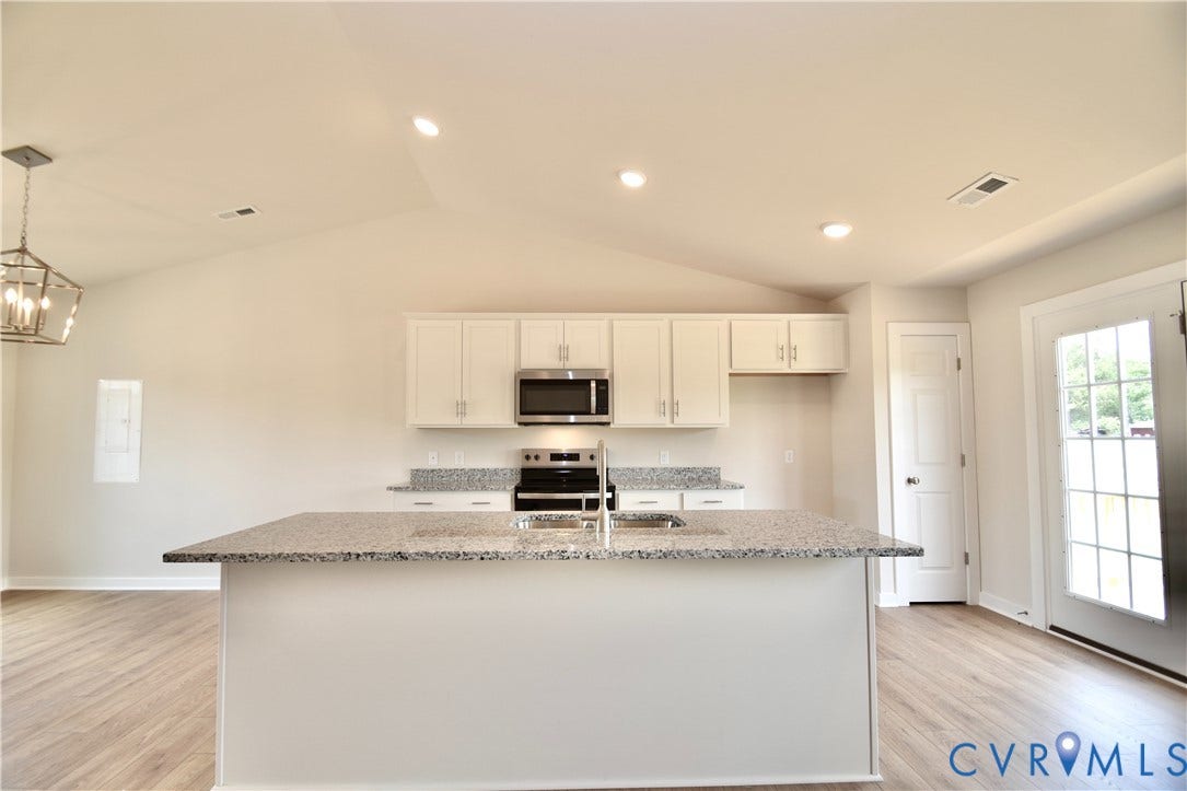 Kitchen featuring a large central island with a granite-style countertop, white cabinetry, and stainless steel appliances