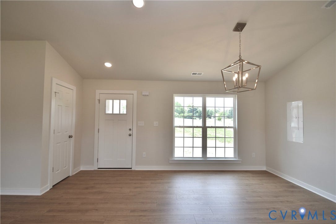 Bright interior space featuring wood-finish flooring, a white paneled entry door with decorative lites, and a large window with white muntins