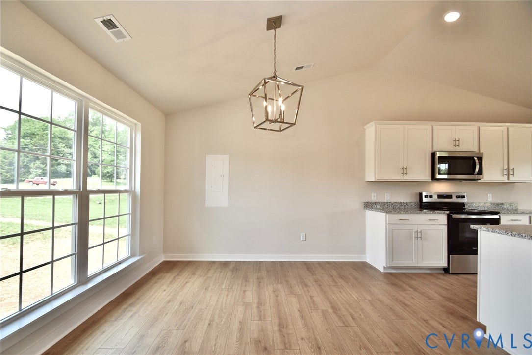 Spacious open-concept room featuring vaulted ceilings, wood-finish flooring, and a contemporary geometric chandelier