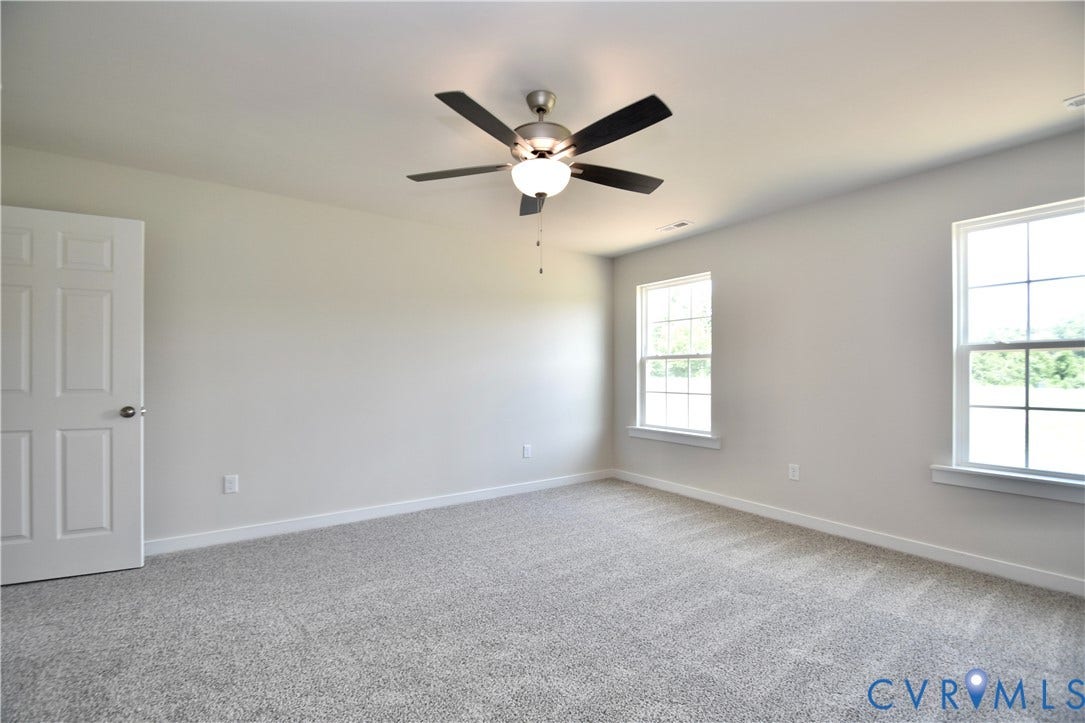 Spacious room featuring new carpet, neutral wall color, two double-hung windows, and a ceiling fan with integrated lighting