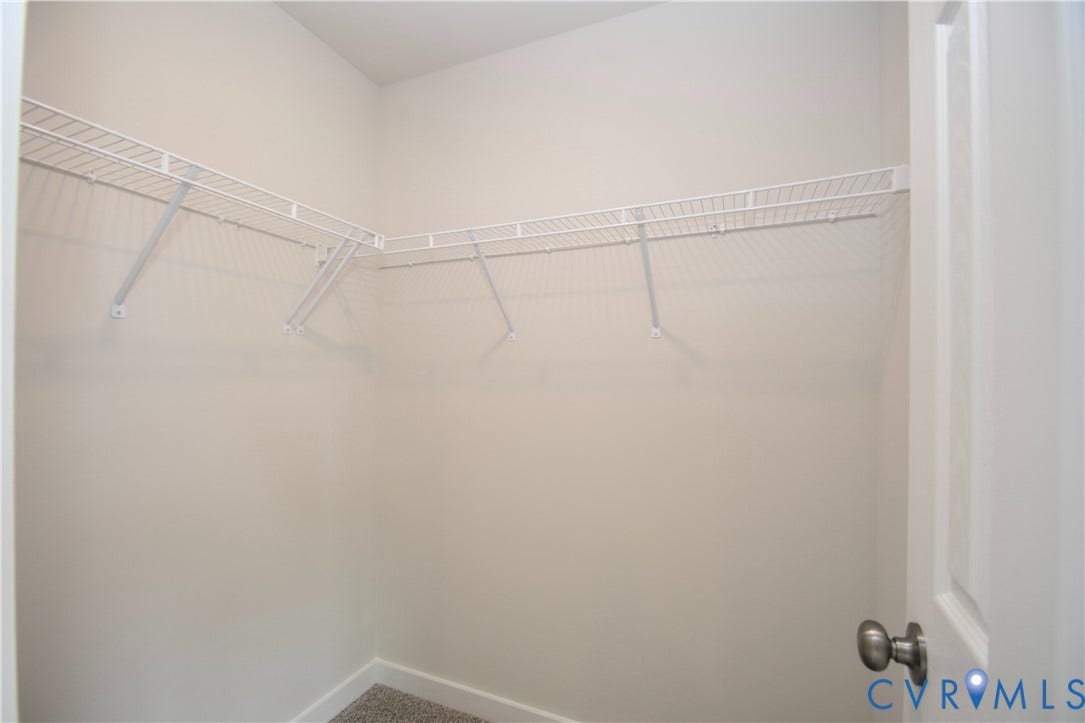 Walk-in closet with L-shaped wire shelving system, light-toned wall paint, and gray carpet