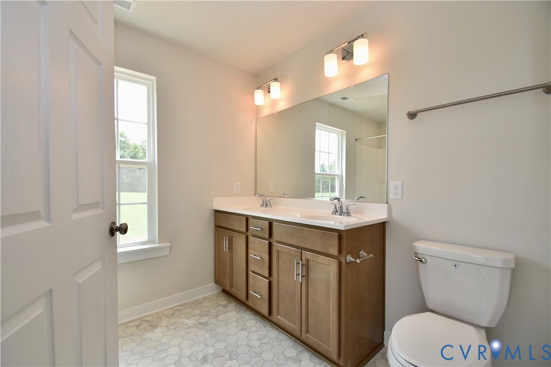 Bathroom featuring a dual vanity with a white countertop and wood-finish cabinetry, hexagonal floor tiling, a single window, and a toilet