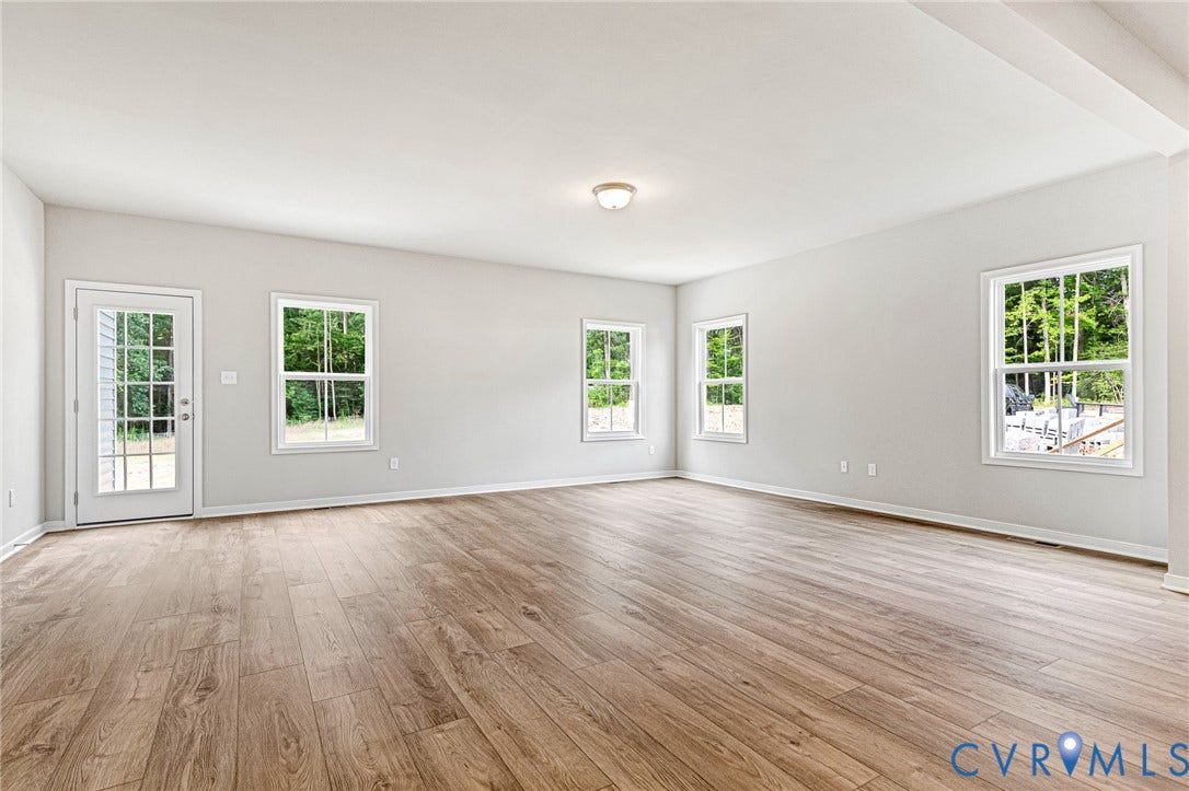 Spacious room featuring wood-finish flooring, light gray walls, white trim, multiple windows, and a glass-paned door