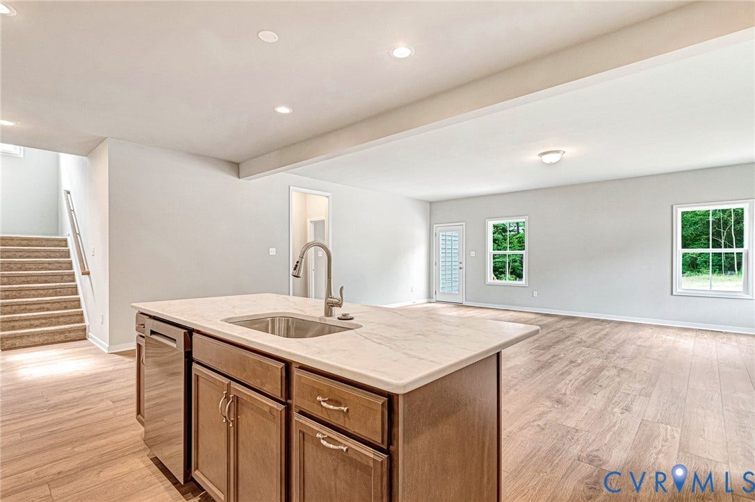 Kitchen island featuring a stainless steel sink with a high-arc faucet, wood cabinetry, and a light-toned countertop