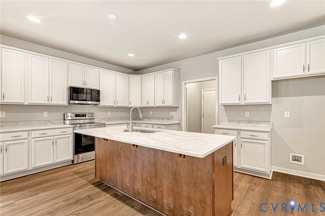Modern kitchen featuring white cabinetry, light countertops, wood-finish flooring, a stainless steel electric range, and a central island with a wood-panel base and integrated sink