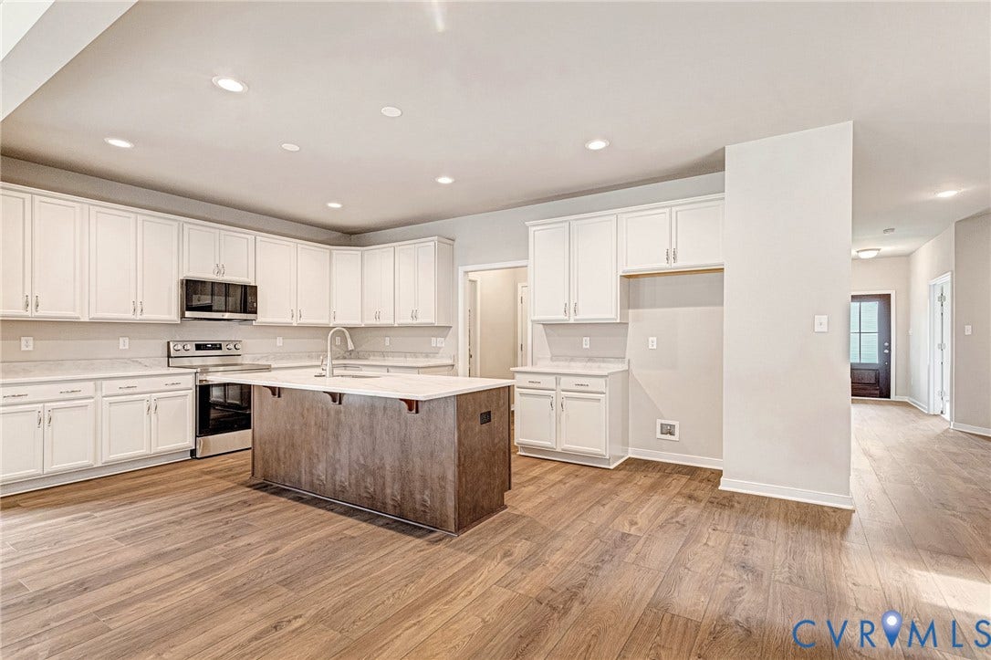 Contemporary kitchen featuring a large central island, white cabinetry, integrated stainless steel appliances, recessed lighting, and wood-finish flooring
